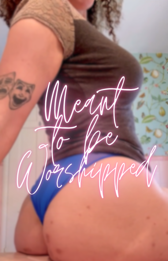 A graphic design of FemDom Goddess Fiestry. The glowing purple text in the foreground says "Meant to Be Worshipped," and the background shows off her curvy, gorgeous, natural body.