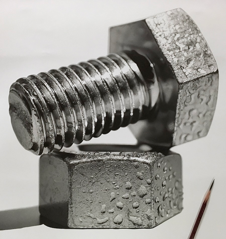 At first glance, this looks like a photograph of a metal nut resting on top of a metal bolt, slightly moist with condensation. In reality, it is a drawing done with pencil. Far in the background on the lower left-hand side, there is a fuzzy image of a pencil.