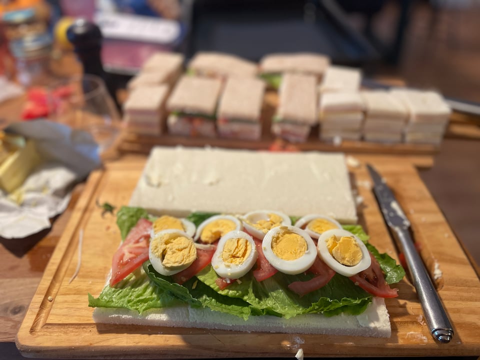 A cutting board is filled with the preparations of homemade miga sandwiches filled with lettuce, sliced tomatoes and egg.