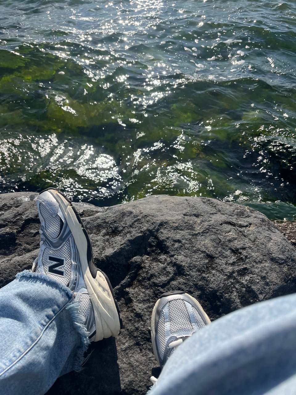 tennis shoes and loose light jeans against a rock above sparkling green water