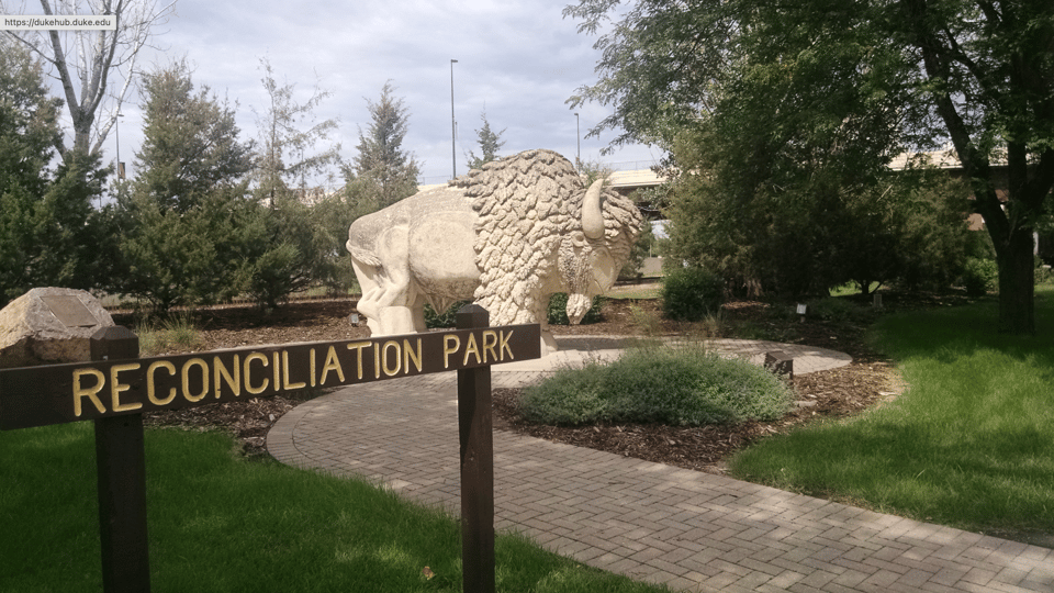 Photo of large off-white stone sculpture of buffalo, with a walkway and sign saying "Reconciliation Park" in the foreground.