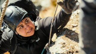 A person in a helmet reaches up over a rock