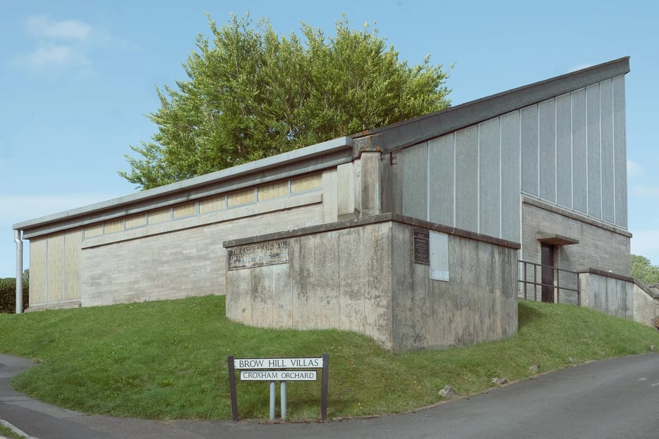 A very plain building whose main feature is the steeply sloping roof in one corner and the grey-cream walls.