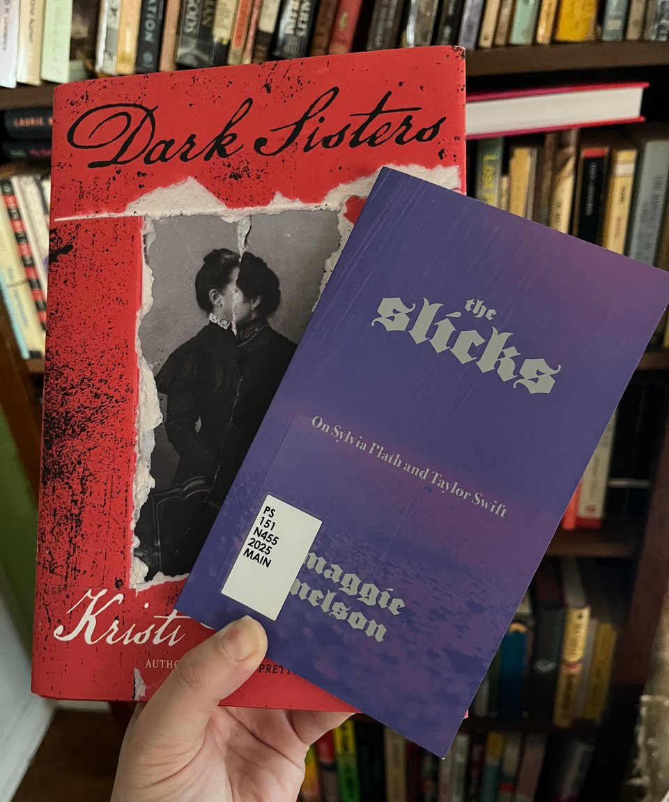 A white person's hand holds two books in front of a bookshelf.