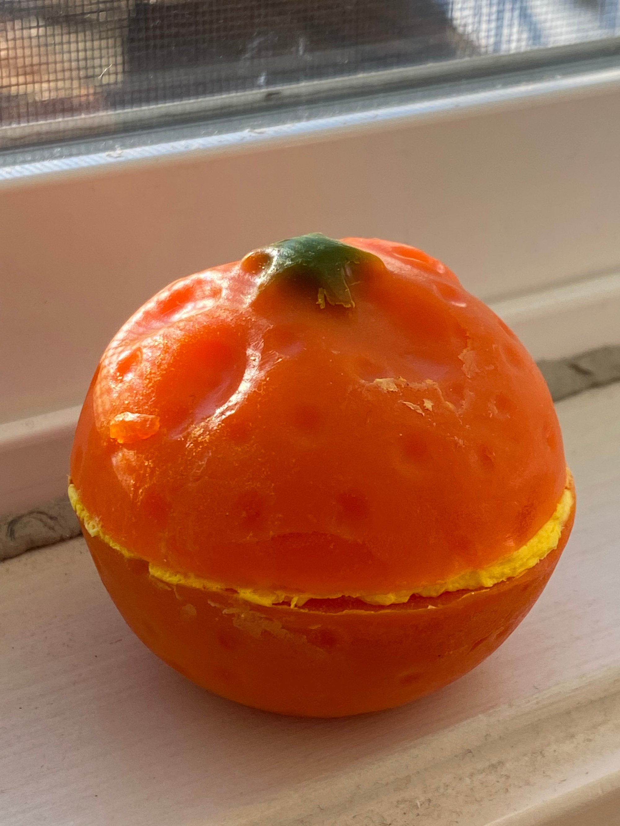 Image of a hunk of soap that is the shape and size of an orange, sitting by the white windowsill in golden hour.