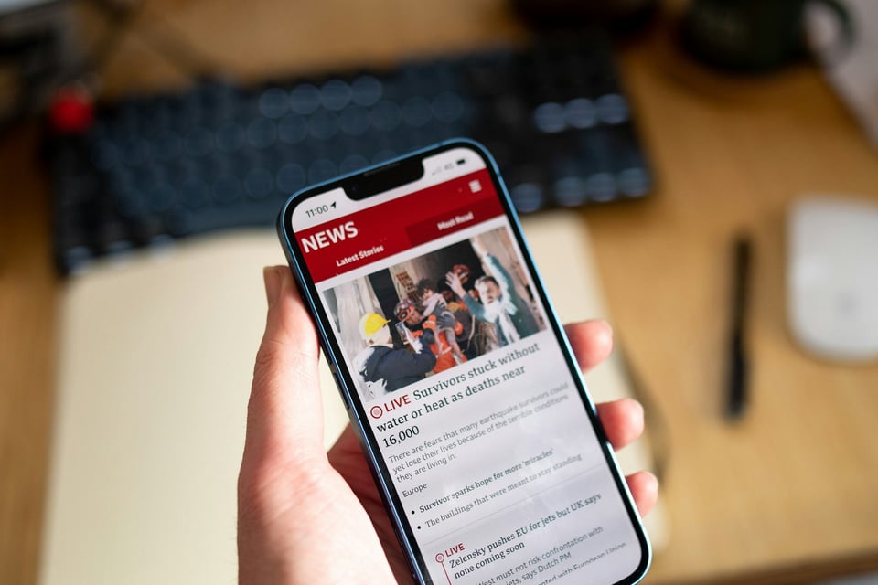 A hand holding a mobile phone, open to a news app. Photo by Rich Tervet on Unsplash