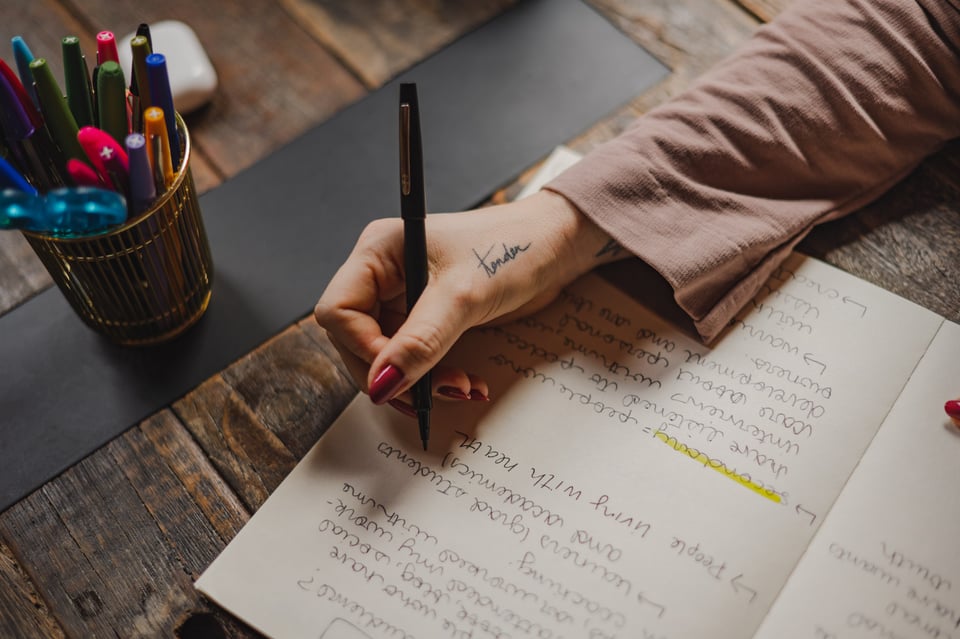 photo of kate's hand with the tattoo of the word "tender." Kate is writing in a notebook