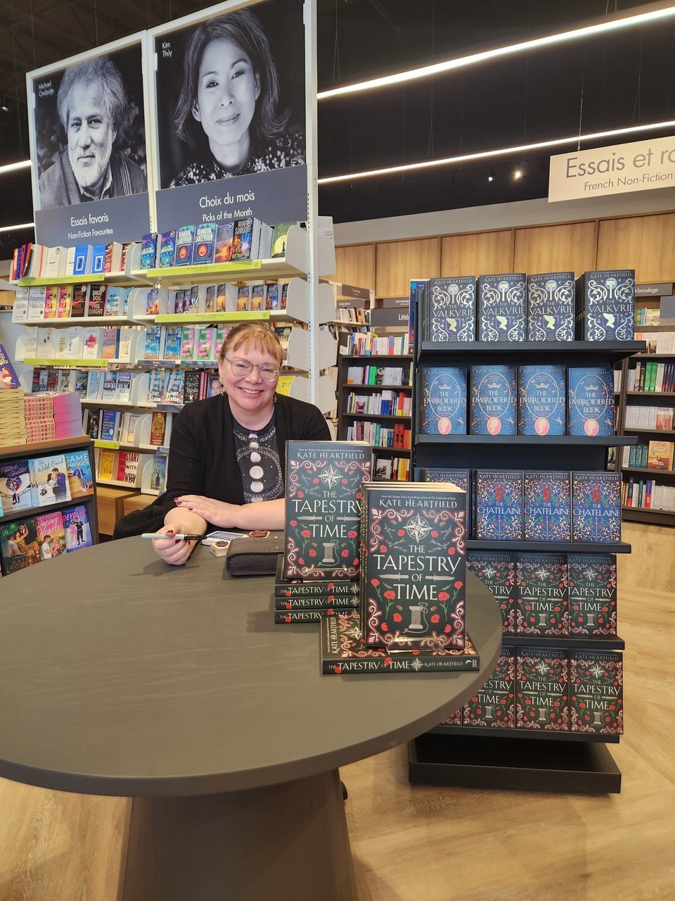 Kate is smiling at a table next to a display of her books.