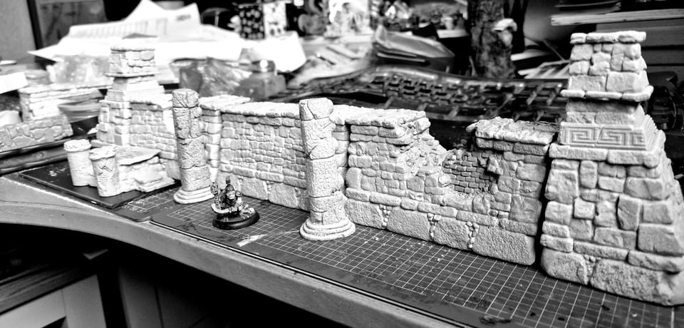 3/4 view in black and white of a set of partially ruined cyclopean stone walls with trapezoidal towers at either end, laid out on a worktop.