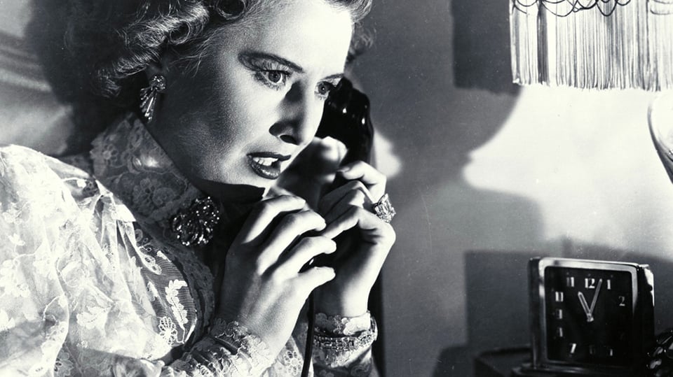Barbara Stanwyck in her nightgown listens to her telephone in distress as two unknown men plot a murder in Sorry, Wrong Number.
