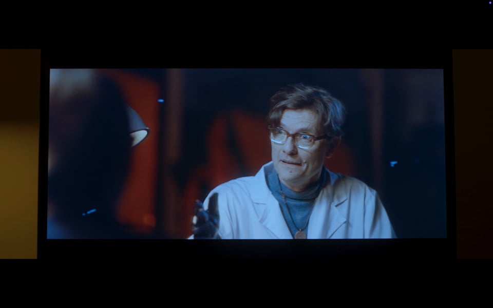 A close-up of a television. On the screen is scratchy film of a mad scientist type gesticulating with fervor