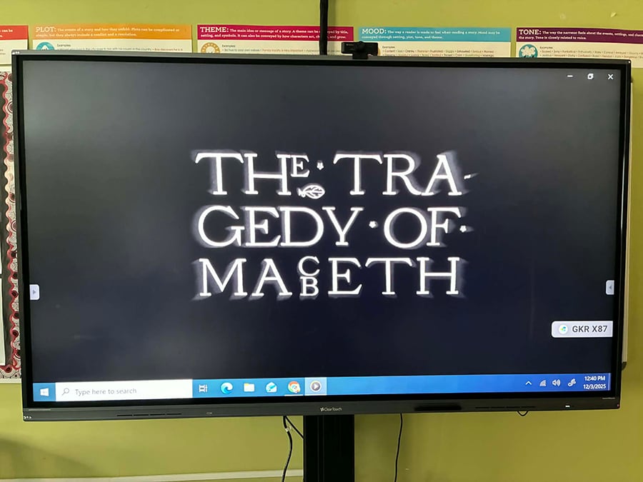 A picture of the computer that's in the front of my classroom. It's a big screen, suitable for showing movies on. The wall behind it is green. On the screen, you see the title of The Tragedy of Macbeth. The spacing of it is weird.