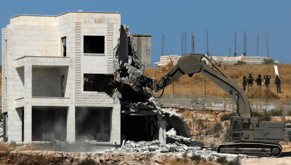 A 3-story stone house, with a bulldozer beginning to demolish the house