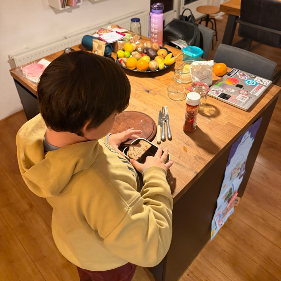 A young boy stands by a kitchen island putting a sandwich into a lunch box.