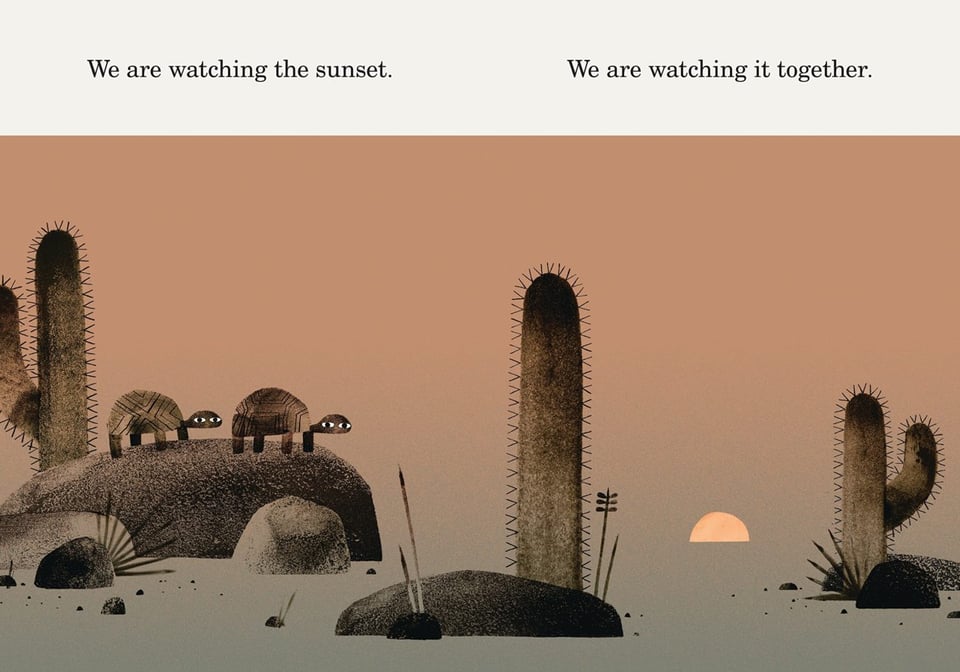 Illustration from a children's book, We Found a Hat. Image: two identical tortises watch the sun set in the desert, stading on a rock, overlooking some cacti. Text: We are watching the sunset. We are watching it together.