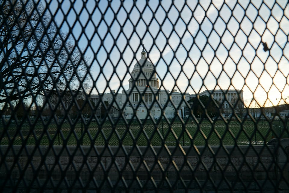 The US Capitol building and iconic dome, slightly out of focus, because it's being seen through a metal security fence with diamond shaped holes.