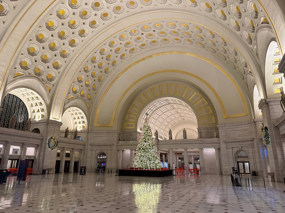 photo of empty main hall of Union Station in Washington, DC, showing arches with gold decor, an illuminated Christmas tree, and not much else