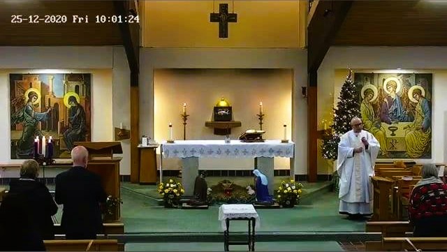 A screenshot showing the alter of the church, lit by candles, as the priest says mass. A datestamp in the corner reveals it is Christmas day.