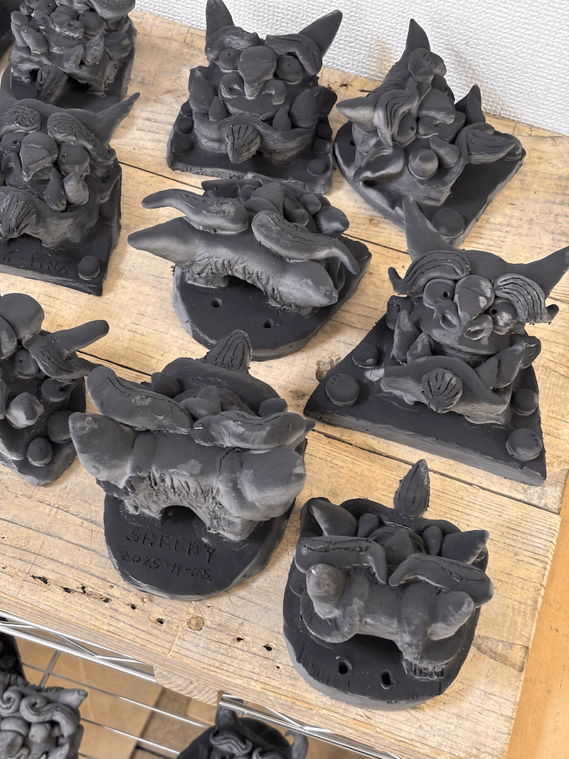 clay figurines on a wooden table; these are a deep, rich grey, and are fiersome so that they scare away bad luck