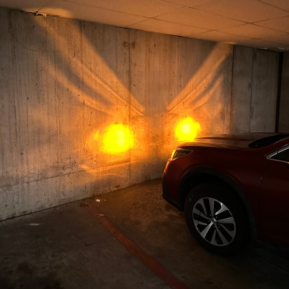 Photo of a concrete parking garage wall reflecting the flashing headlights of a Subaru Outback in a way that looks like a pair of bright orange wings