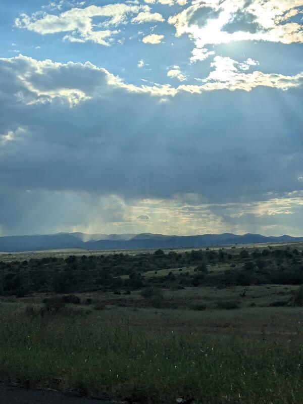 Rainclouds over distant mpuntains and sun rays over a shrubby plain
