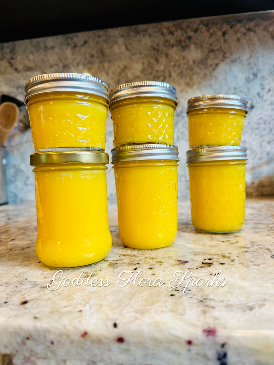 6 glass jars of bright yellow lemon curd on a marble counter