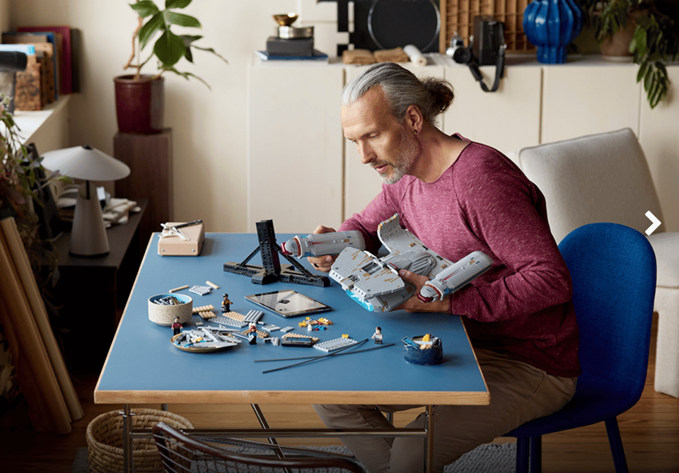 Photo of white man with long hair tied back and a well-trimmed beard, assembling a Lego version of the starship Enterprise