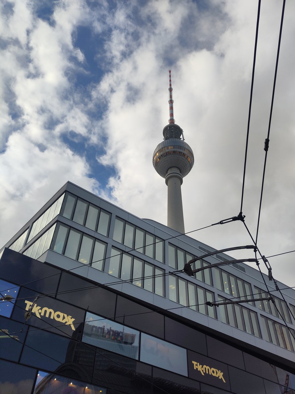 Blick auf den berliner Fernsehturm vor bewölktem Himmel, im Vordergrund eine Schwarz glänzende Shopping-Mall.