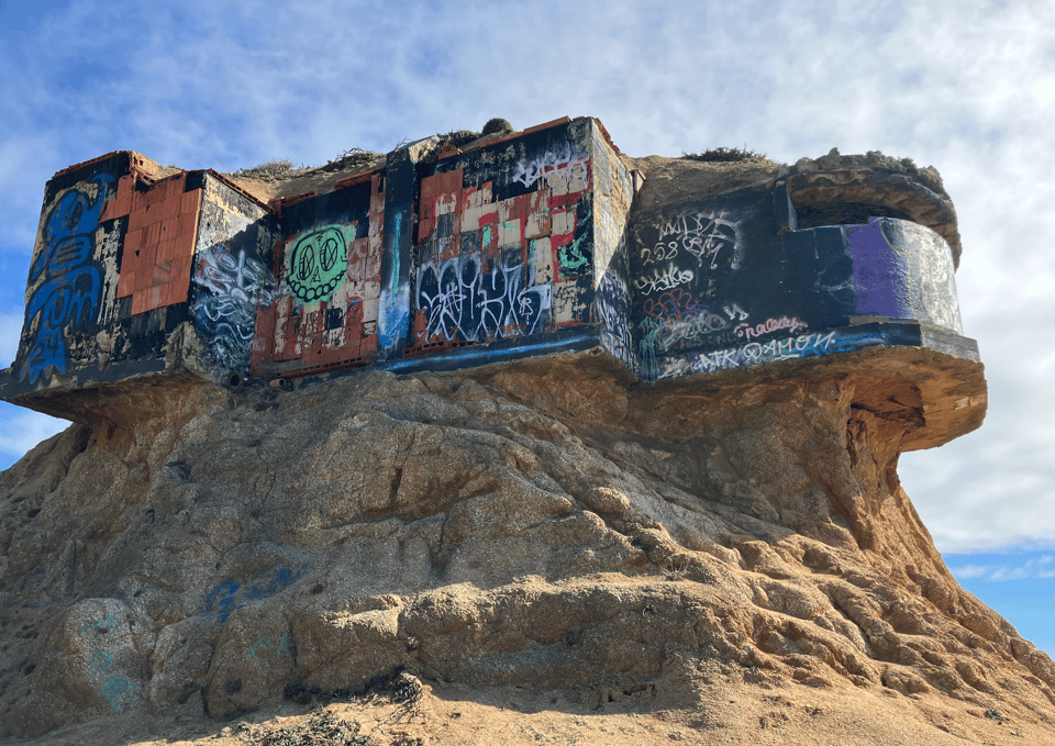 an old WWI or WWII bunker is covered in graffiti and perched on top of a seaside cliff.