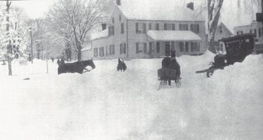 grainy historical photo showing three different horses, two clearly pulling sleighs, and an automobile appearing stranded. there are several feet of snow