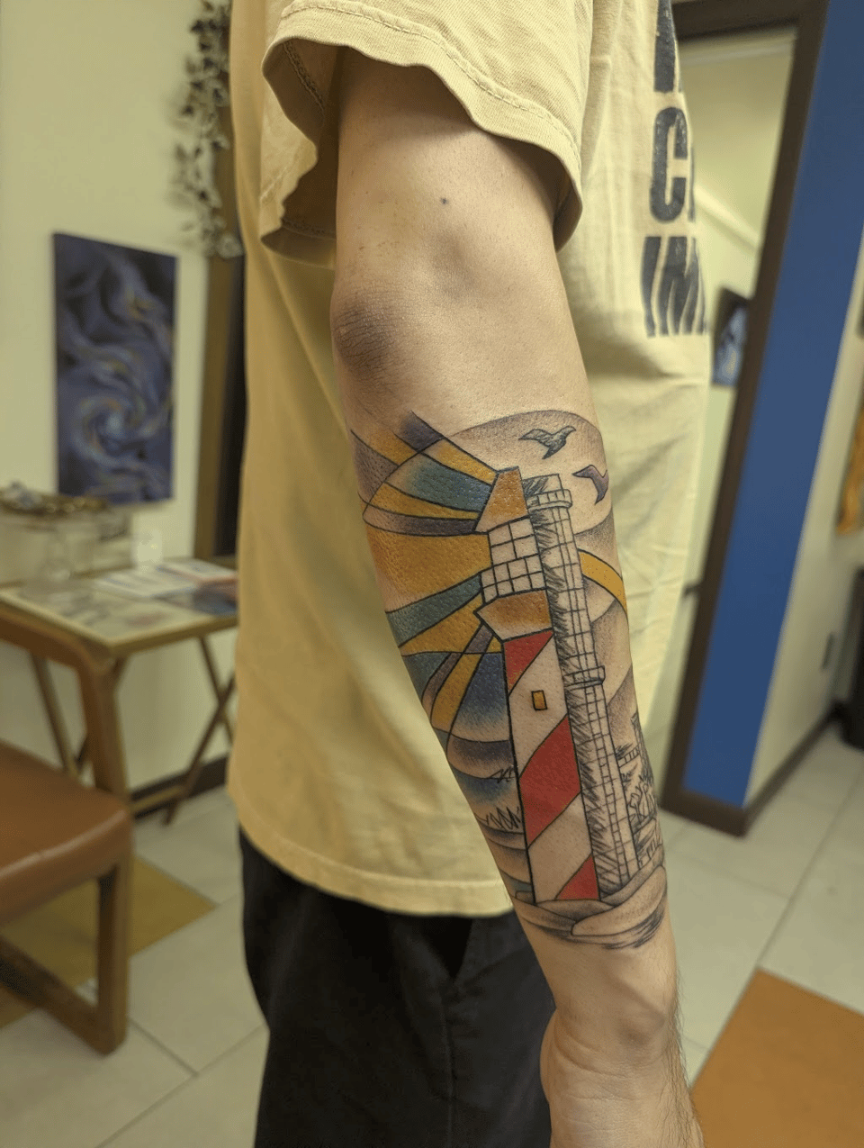 On the right, a stained glass lighthouse tattoo that transitions into a black & grey tattoo of Cementland with a more drawn aesthetic.