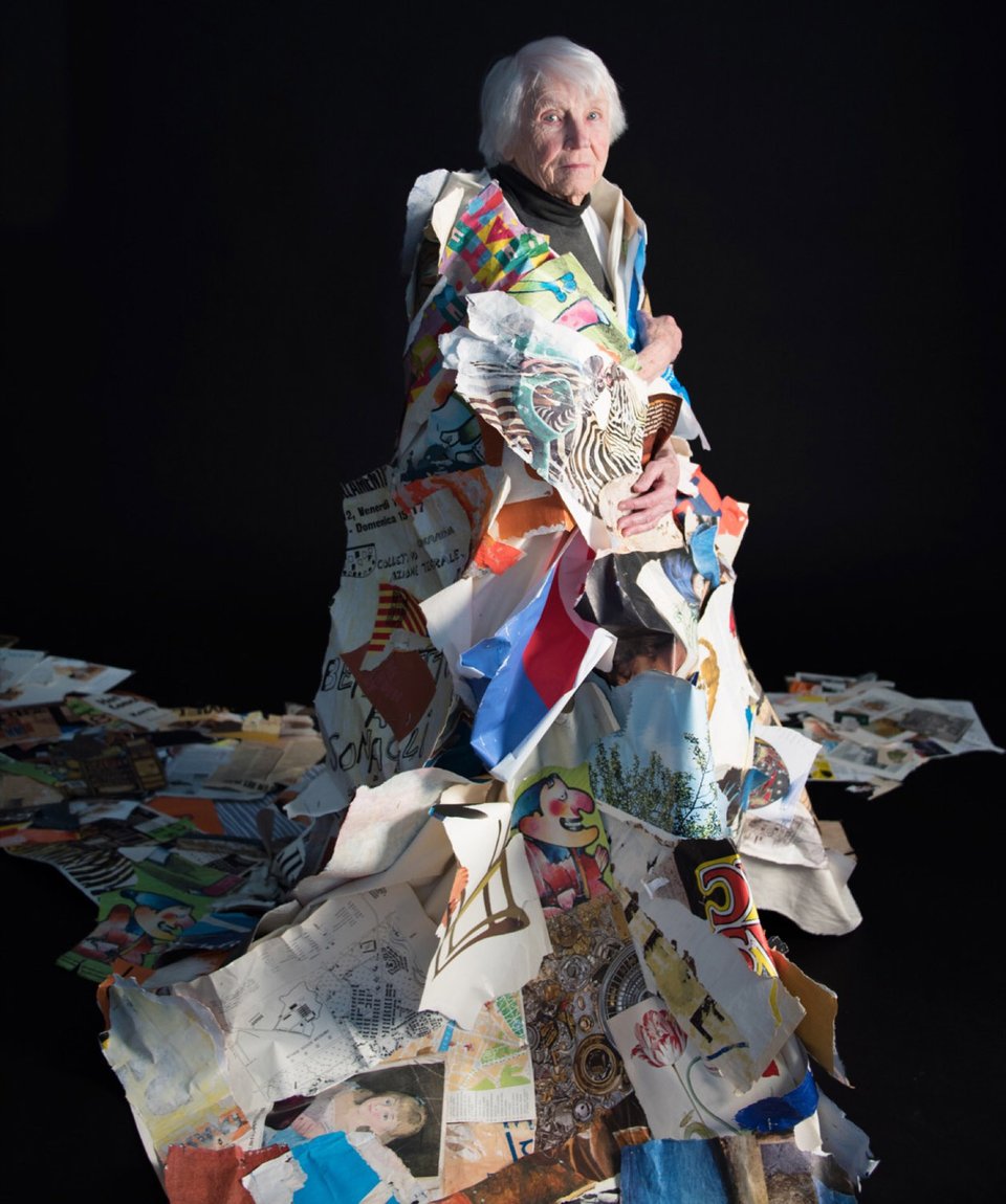 A portrait of Eunice Parsons at age 100 wrapped in a gown of paper collage materials in front of a black background.