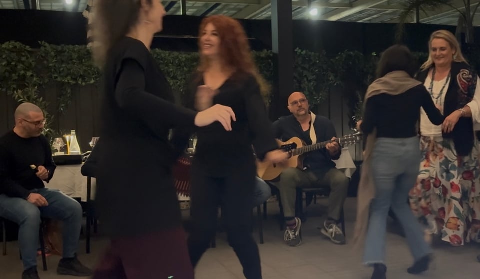 Four smiling people dance pizzica as musicians play