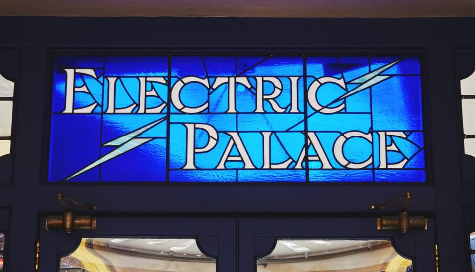 A panel of stained glass containing the words Electric Palace in white on a electric blue background. There are two white lightning bolts as well.