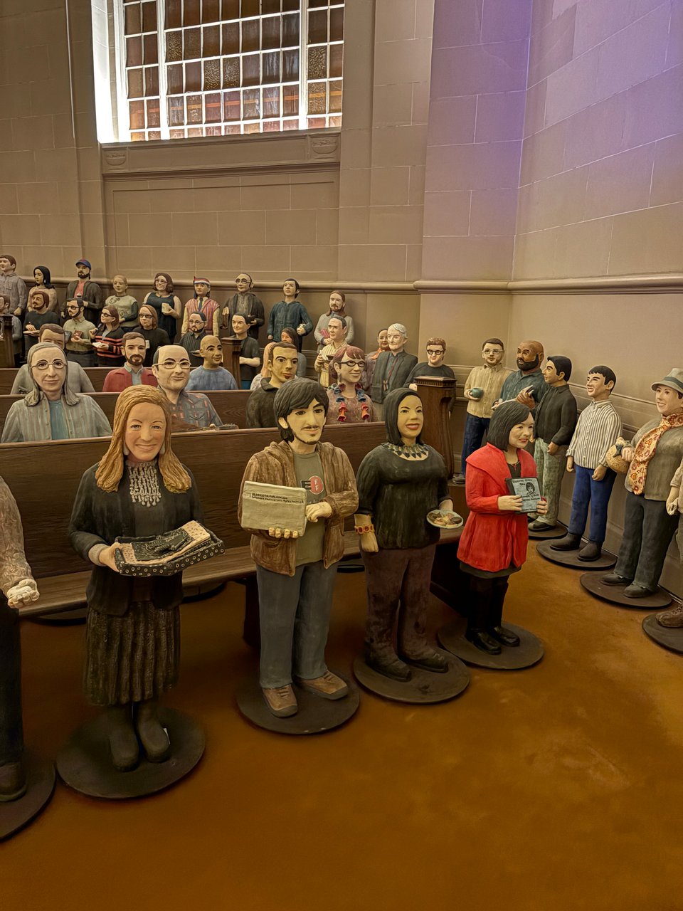 Alt text: Lots of statues of people in front of church-like pews.