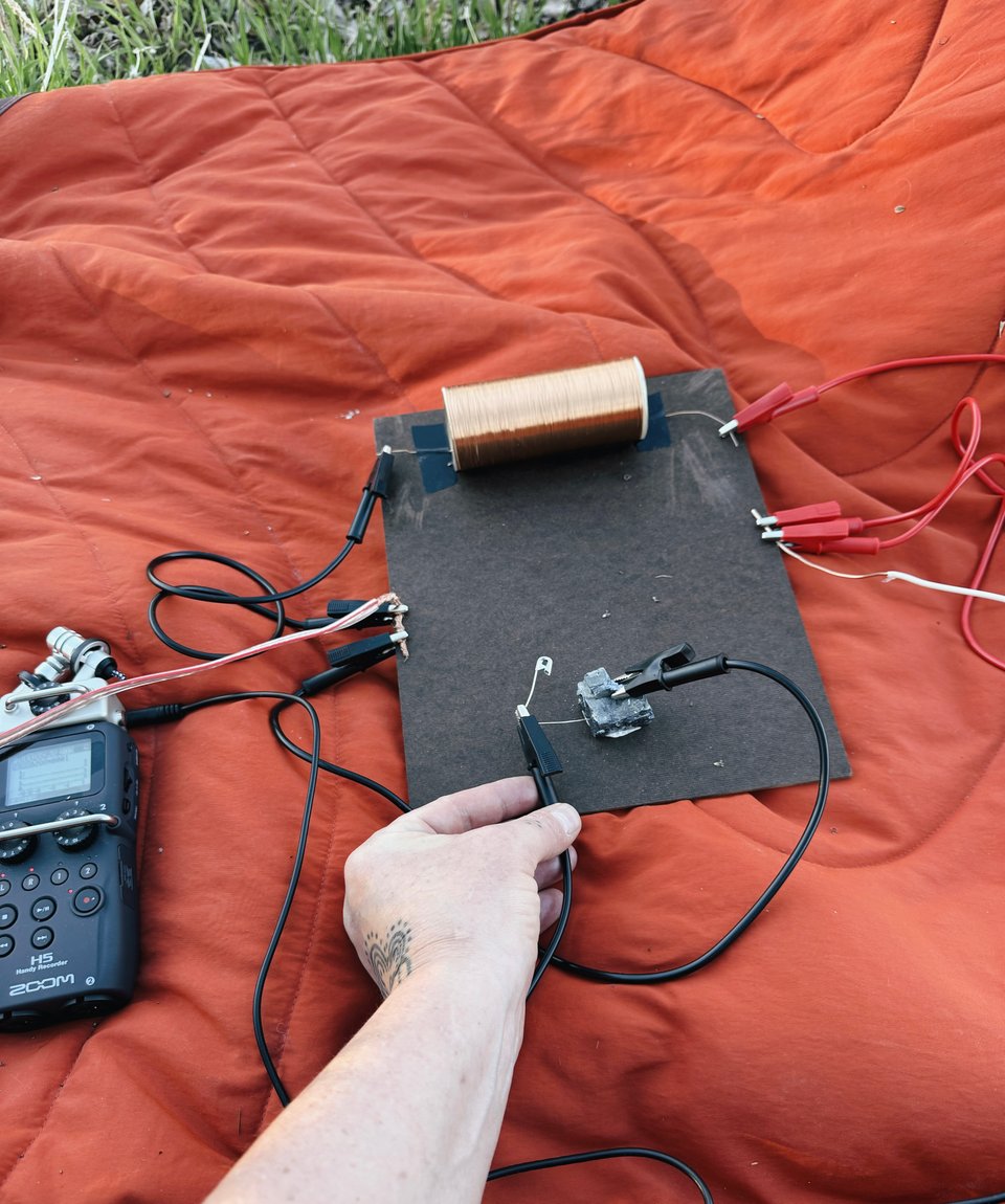orange blanket with an open wave receiver, a hand holds an alligator clip with a cat's whisker touching a diode on the receiver.
