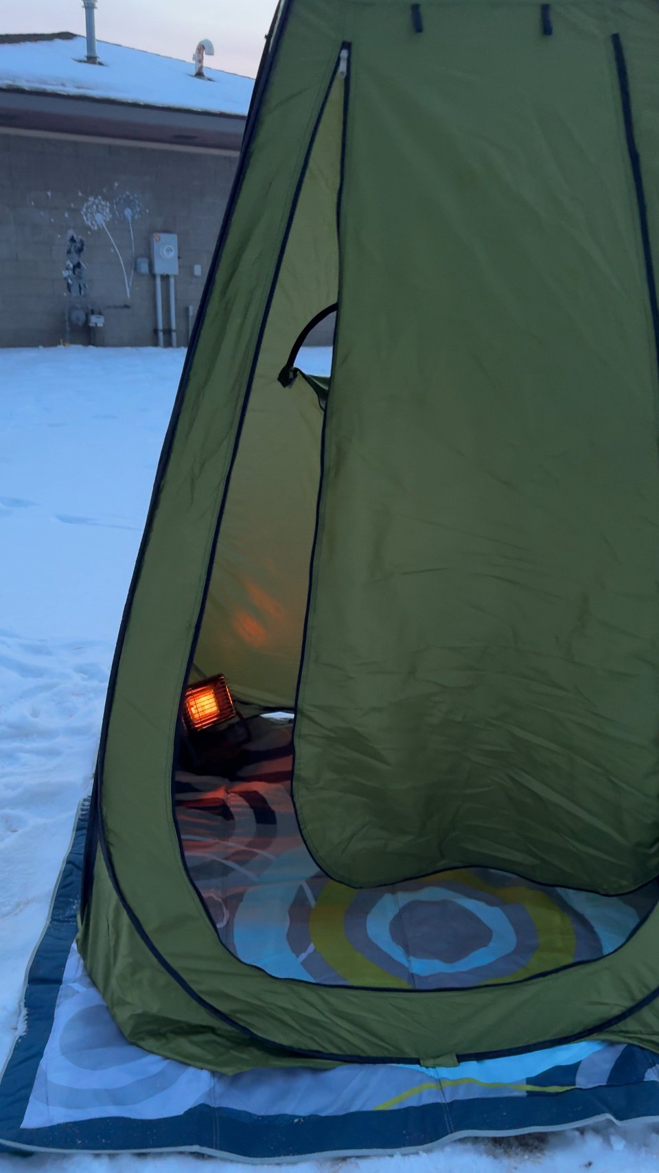 Photo of green camping shelter sitting on top of a patterned weatherproof blanket in the snow