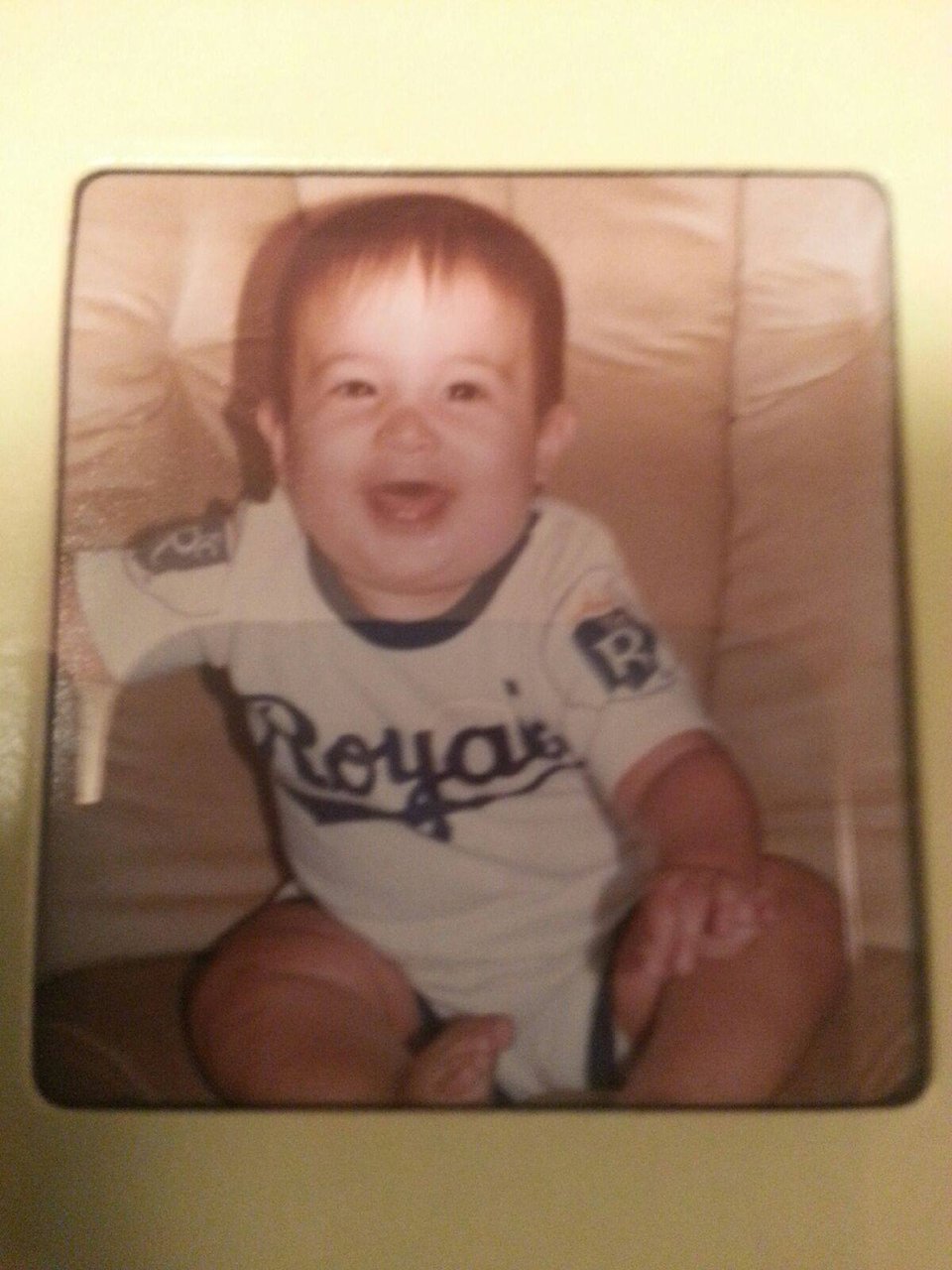 a young baby wearing a KC Royals onesie and smiling in a chair