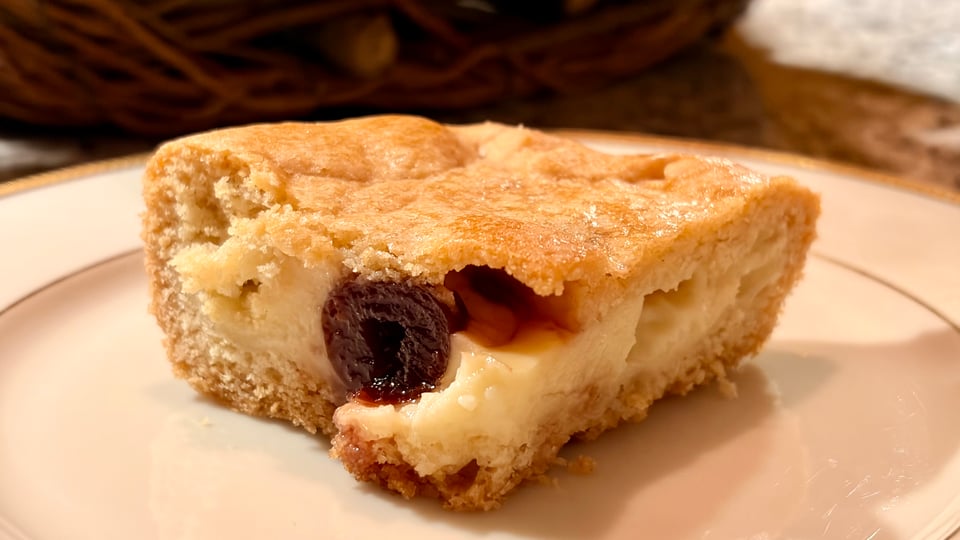 A square of custard tart with a half candied sour cherry in the middle