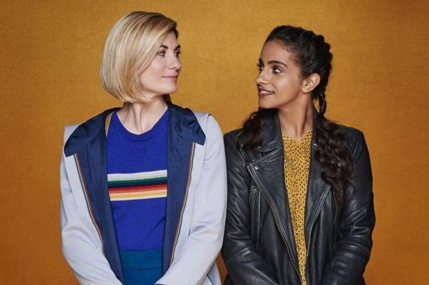 The 13th Doctor and Yaz, shoulder to shoulder, smiling at one another fondly.
