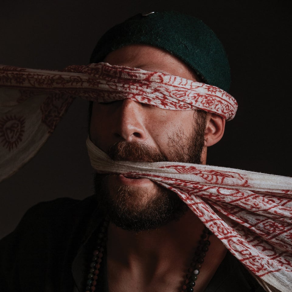 a man in traditional Iranian dress is intriguingly blindfolded and gagged by the same long scarf