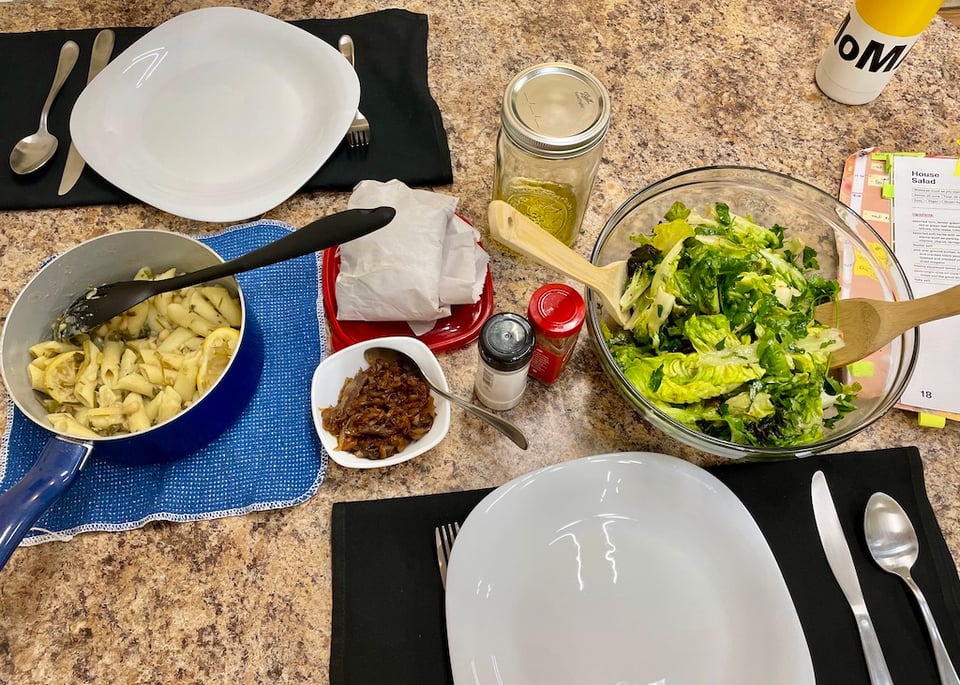 A table laid for two, with salad leaves in a bowl along with pasta and onion