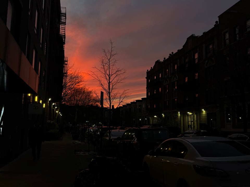 A sunset on a Brooklyn street. The sky is colored in pinks, yellows, and blues.