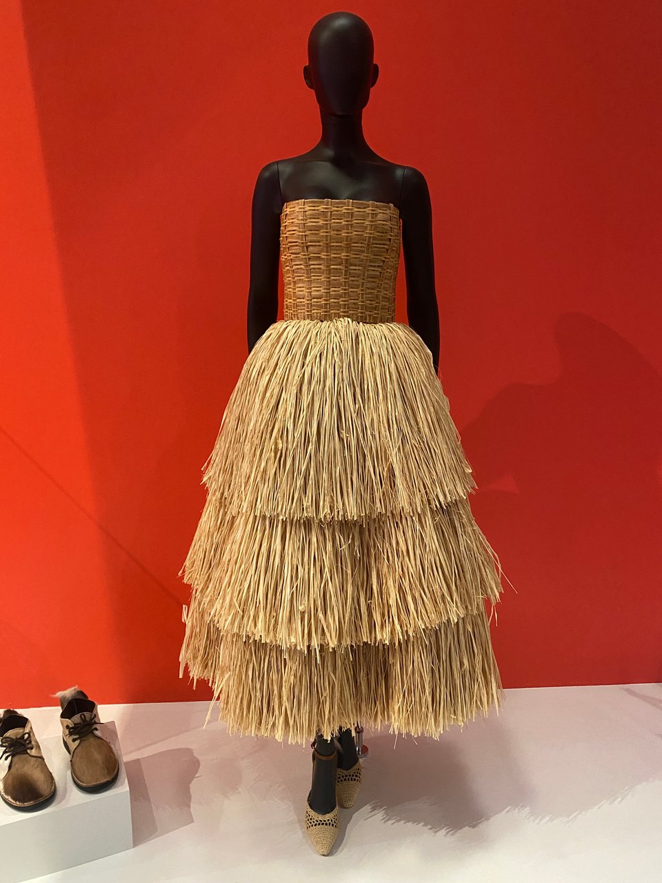 A mannequin wearing a strapless dress made out of raffia, with a tight bodice and tiered skirt