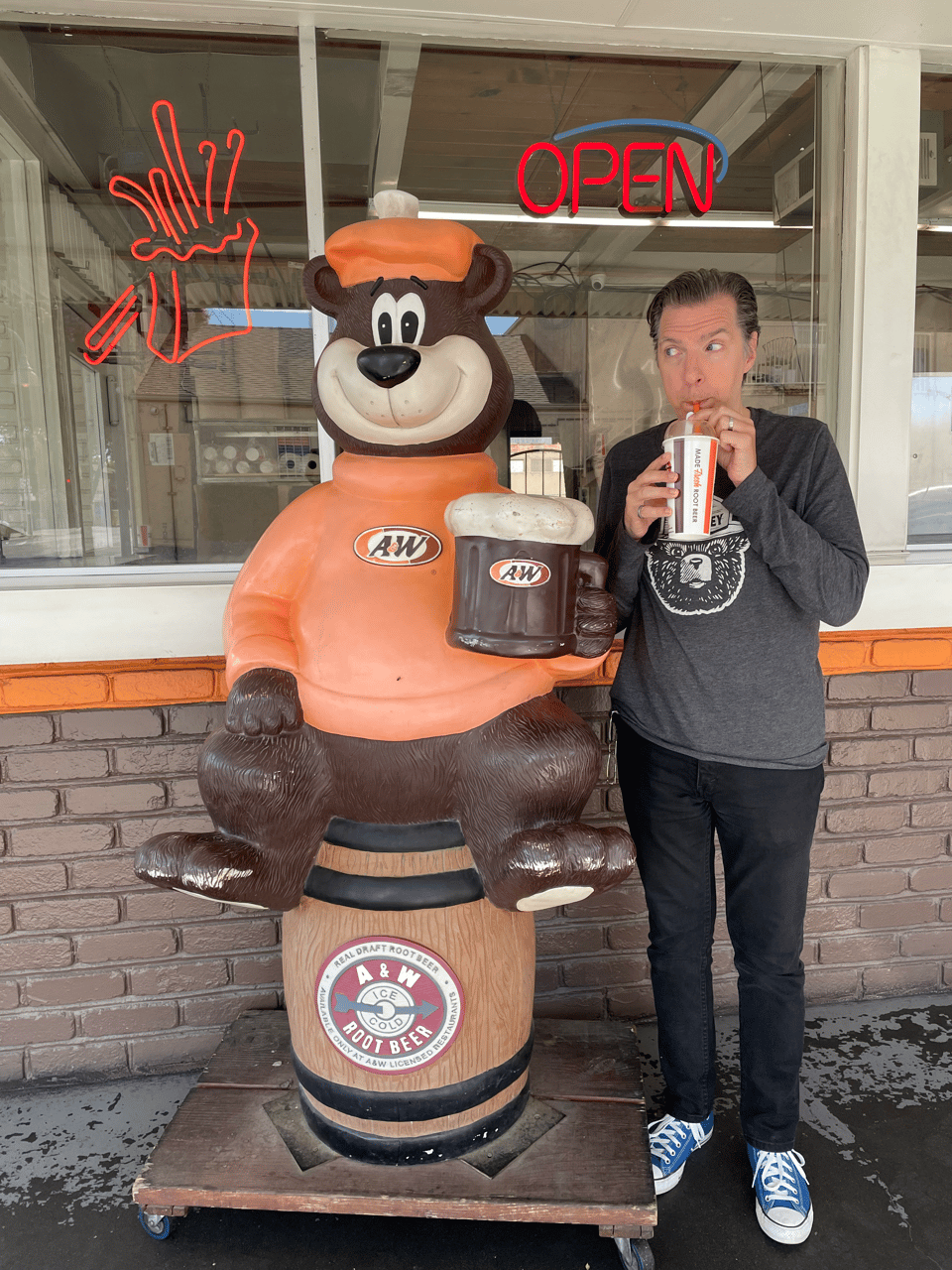 A man slurps a root beer float standing next to a statue of a bear holding a root beer float