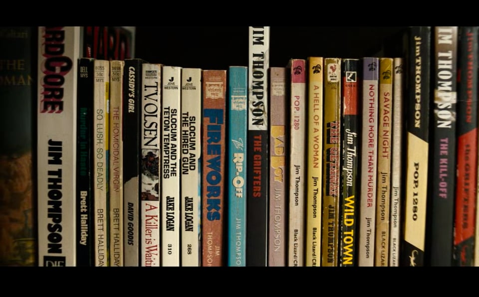 Bookshelf showing spines of various books including Jim Thompson, Jim Thompson's Wild Town, Nothing More Than Murder, Savage Night, A Hell of a Woman, and other noir and literary titles arranged vertically