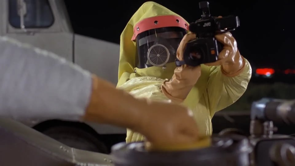 Marty wears a radiation suit and holds up a camcorder as Doc unseals the nuclear component of the time machine.