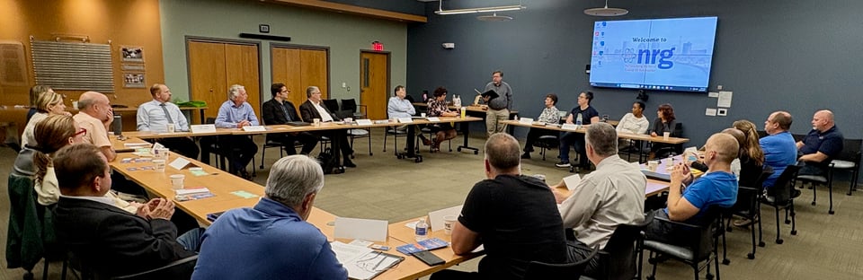 Paul Tracy stands in front of a room and speaks to seated NRG members and visitors.