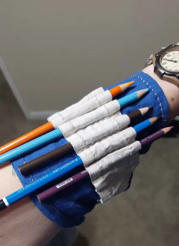 An arm, wrapped with a fabric gauntlet with holes for pencils and a number of pencils within them!
