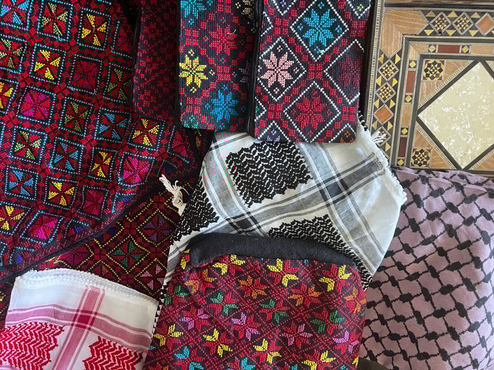 A colorful assortment of handicrafts - embroidery, kuffiyehs (red, black, and purple), an inlaid wooden tray, etc.
